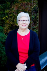 Jennifer Spearman, Insurance Coordinator at Elite Eye Care in Arden, NC, seated in front of an autumn wooded background. She smiles warmly, wearing glasses and a bright red shirt.