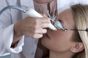 Image of a doctor holding the Optilight probe near the lower left eyelid of a patient wearing protective eye goggles.